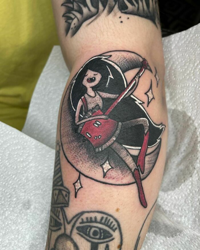 Cartoon tattoo featuring a character with a red guitar sitting on a crescent moon, evoking childhood favorites.