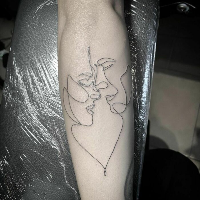 Single-line tattoo of two faces kissing, showcasing minimalist art on an arm.