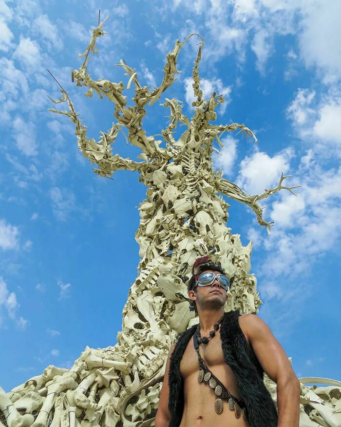 Man taking photo in front of statue made form bones 