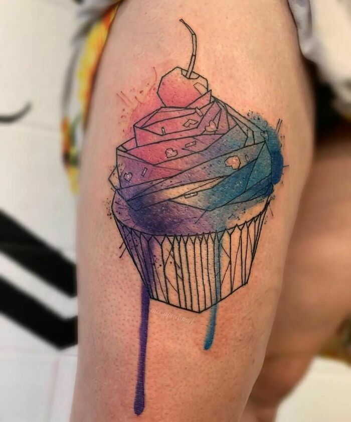 Watercolor tattoo of a cupcake with geometric shapes and vibrant colors on a person's arm.