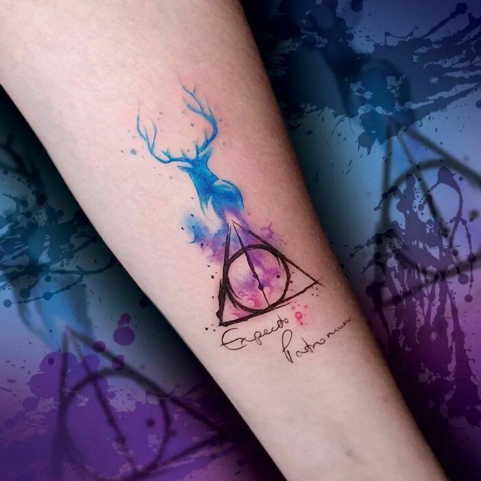 Harry Potter tattoo with Deathly Hallows symbol and a stag Patronus on arm, featuring vibrant watercolor effect.