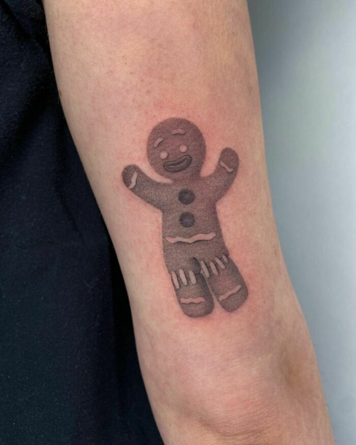 Cartoon tattoo of a cheerful gingerbread man on an arm, evoking childhood favorites.