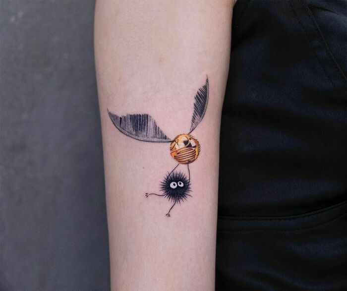 Harry Potter tattoo featuring a Golden Snitch with a black fuzzy creature on an arm for wizarding world fans.