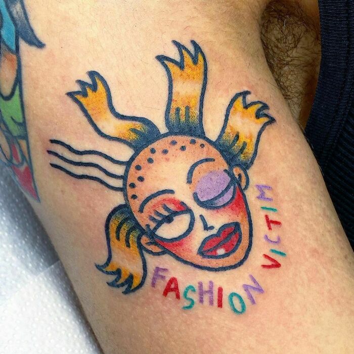 Colorful cartoon tattoo of a stylized face with "Fashion Victim" text.