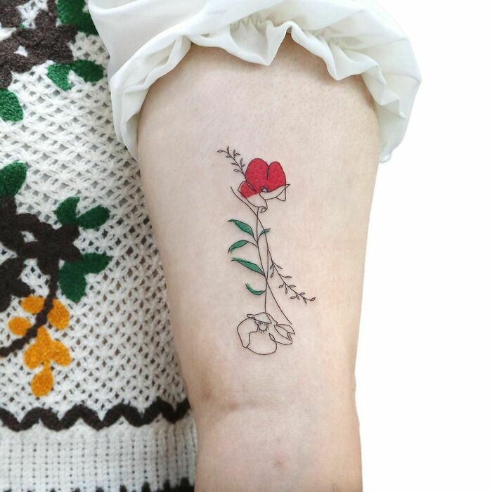 Fine-line single-line tattoo of a flower with red petals and green leaves on upper arm.
