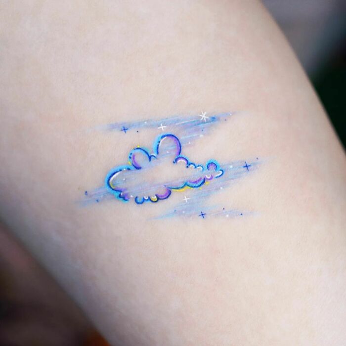 Watercolor tattoo of a cloud with blue and rainbow hues on skin.