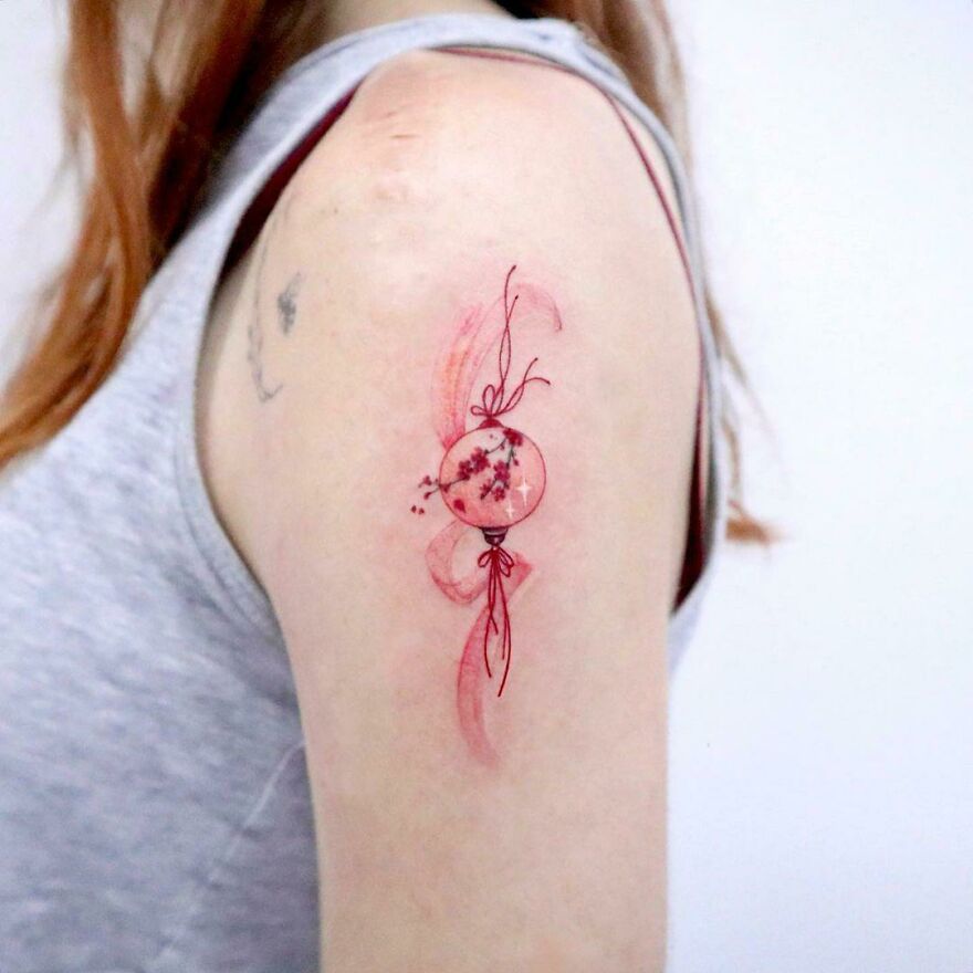 Watercolor tattoo design on upper arm featuring abstract pink and red floral elements.