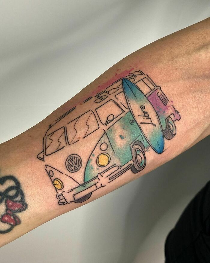 Watercolor tattoo of a van and surfboard on an arm, showcasing vibrant blue and pink ink.