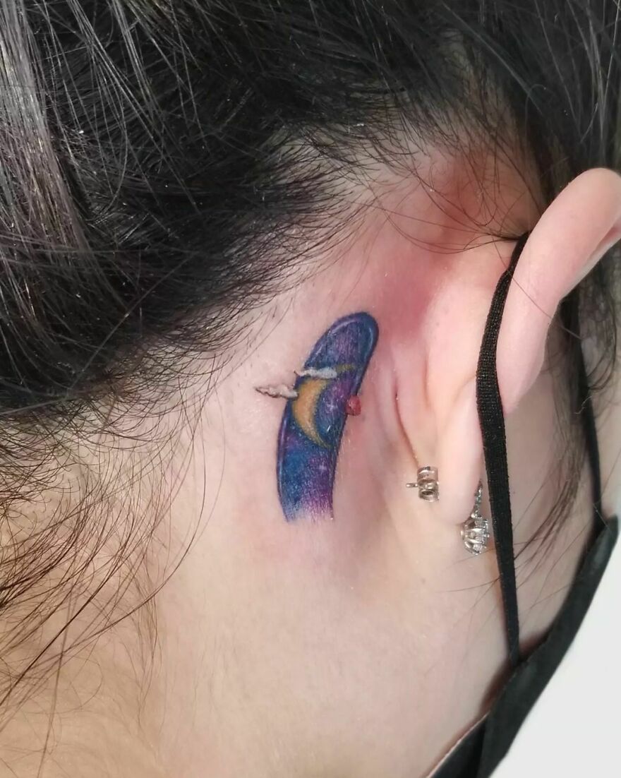Watercolor tattoo of a space scene behind the ear, featuring vibrant colors and a planet design.