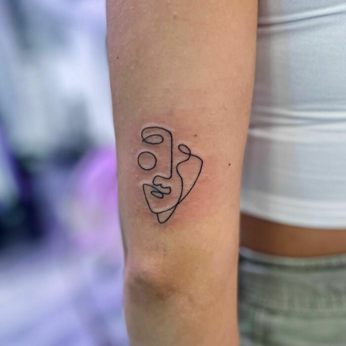 Minimalist line tattoo of an abstract face on a person's arm.