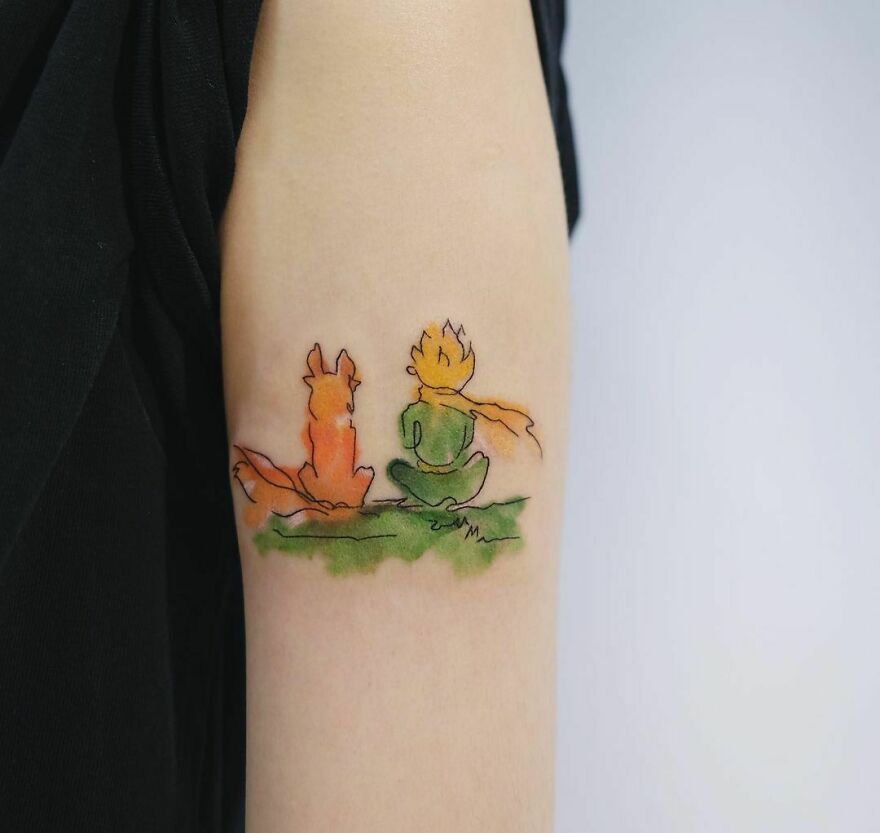 Watercolor tattoo of a fox and a seated figure on an arm, featuring vibrant greens and oranges.