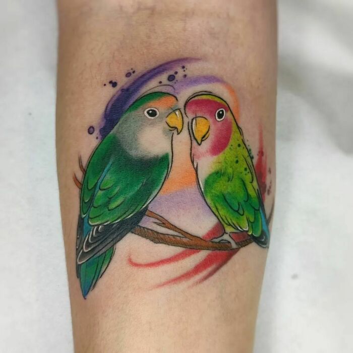 Vibrant watercolor tattoo of two lovebirds perched on a branch.