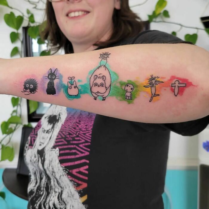 Colorful watercolor tattoo featuring animated characters on a person's forearm.