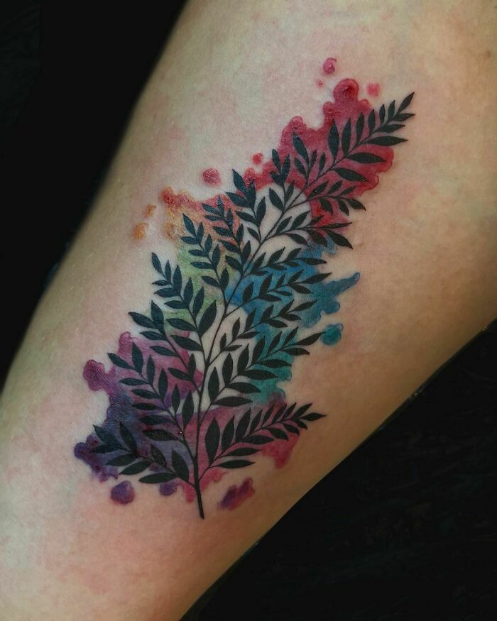 Watercolor tattoo of a colorful fern on skin, blending vibrant hues for inkspiration.