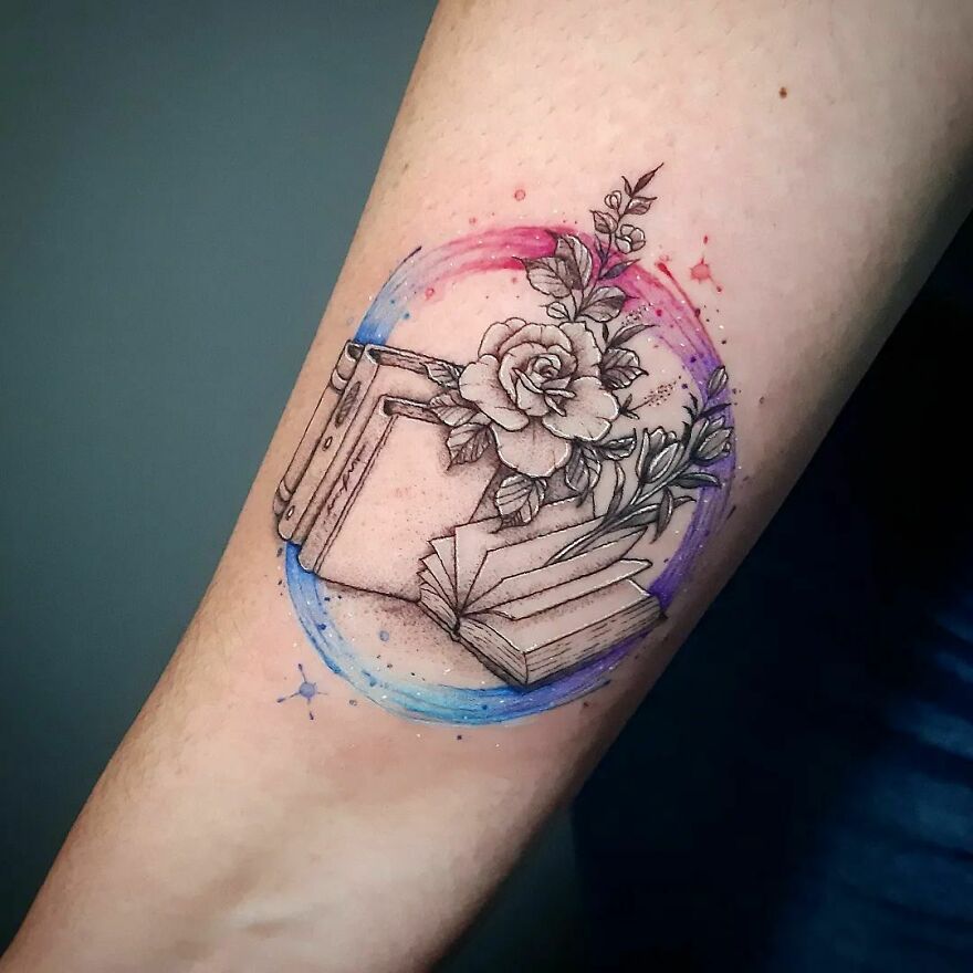 Watercolor tattoo of books and a rose with colorful splashes on the arm.