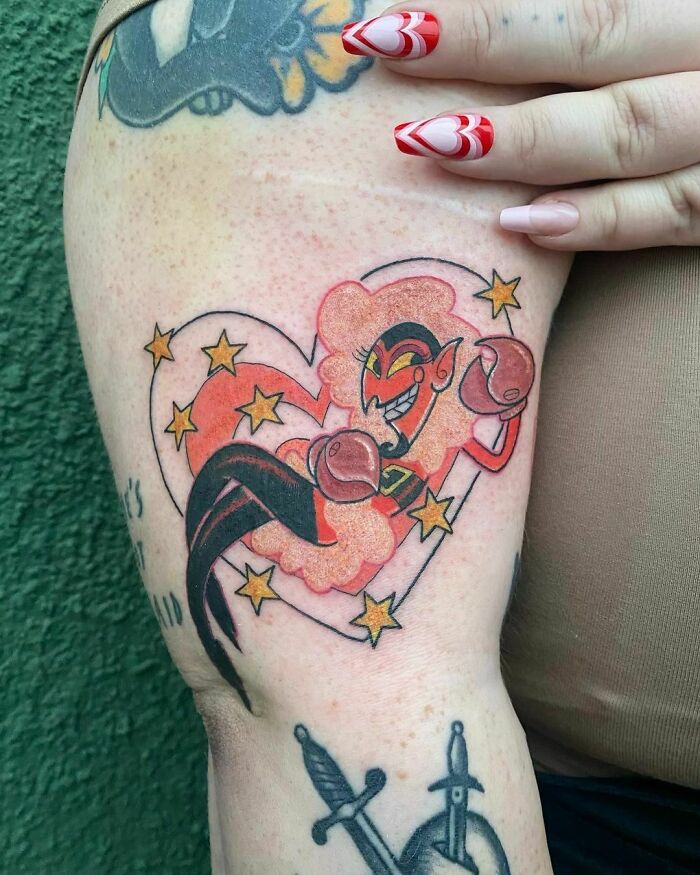 Cartoon tattoo featuring a colorful, whimsical character with stars and a heart on an arm, evoking childhood favorites.
