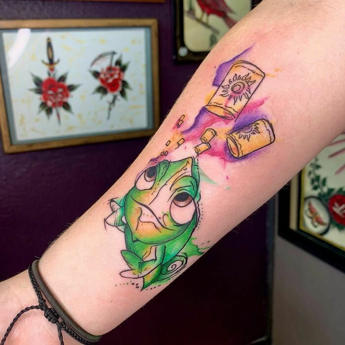 Watercolor tattoo of a green chameleon on an arm, featuring vibrant colors and playful design elements.
