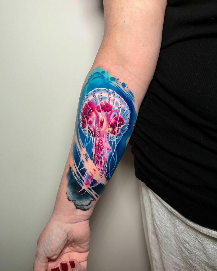 Colorful jellyfish watercolor tattoo on forearm, blending vibrant pinks and blues for inkspiration.