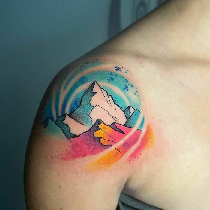Ethereal watercolor tattoo of mountains with colorful, swirling design on a shoulder.