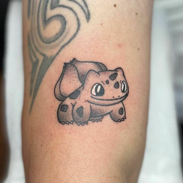 Cartoon tattoo of a smiling creature with spots and a leafy back on a person's arm.