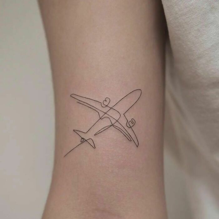Fine-line single-line tattoo of an airplane on an arm.