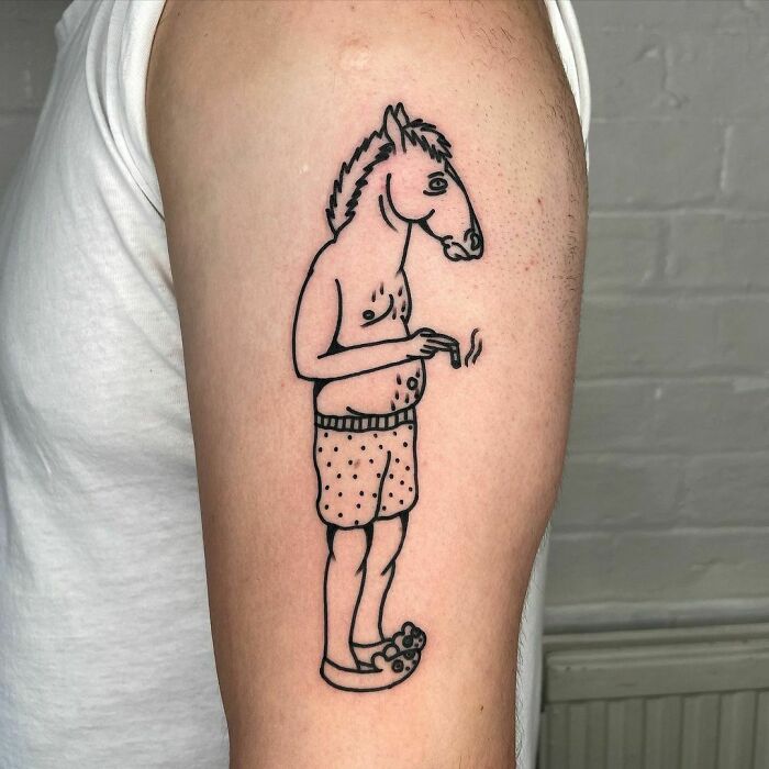 Cartoon tattoo of a human with a horse head, wearing boxers and slippers, on upper arm.