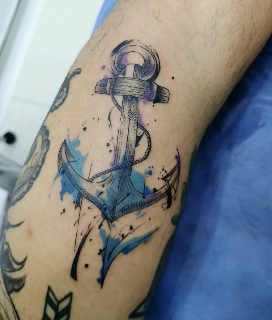 Watercolor tattoo of an anchor with blue splashes, showcasing a creative and artistic design.
