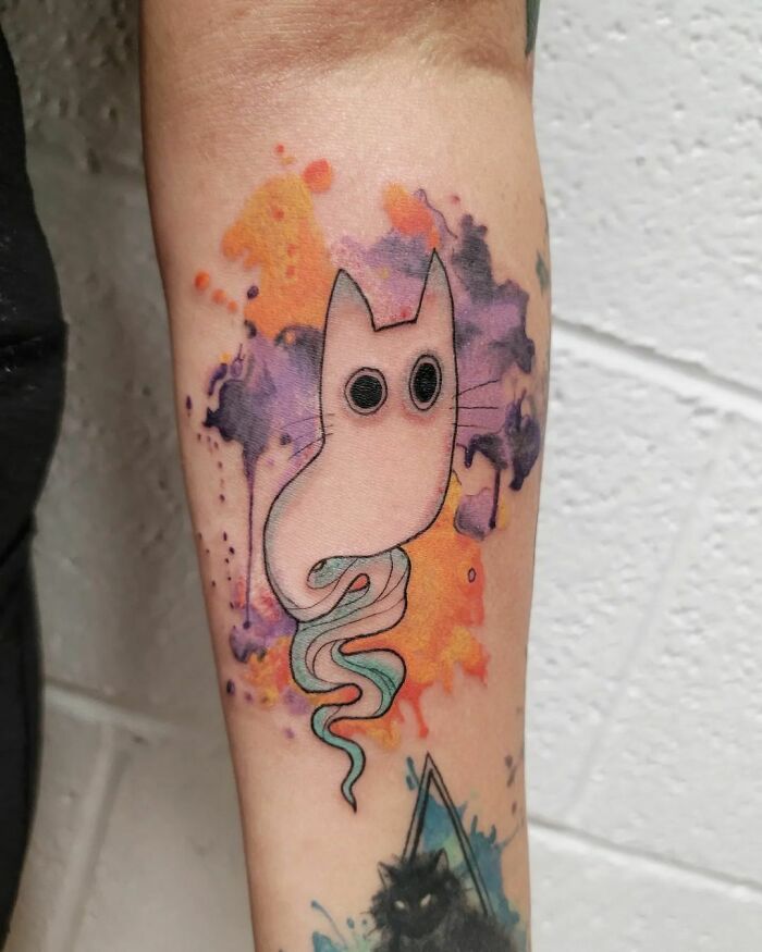 Abstract cat watercolor tattoo with vibrant splashes of orange and purple on forearm.
