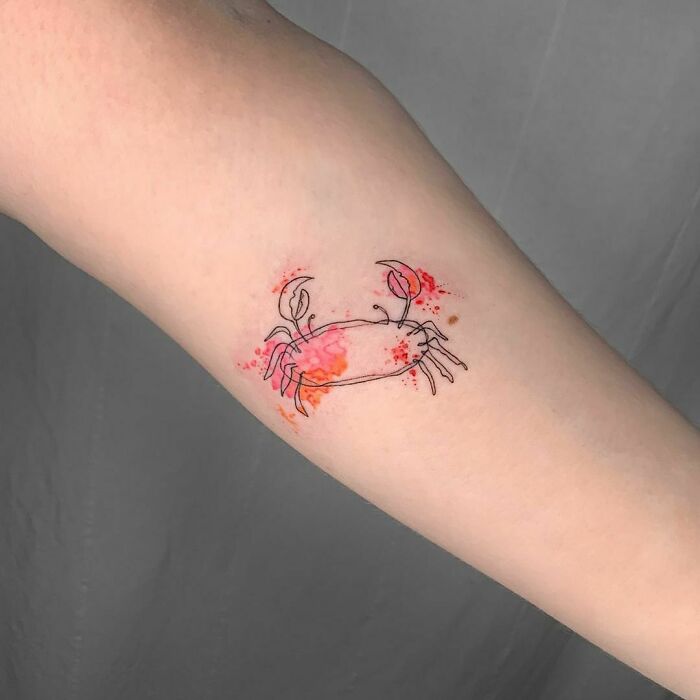 Minimalist watercolor tattoo of a crab with splashes of red and orange ink.