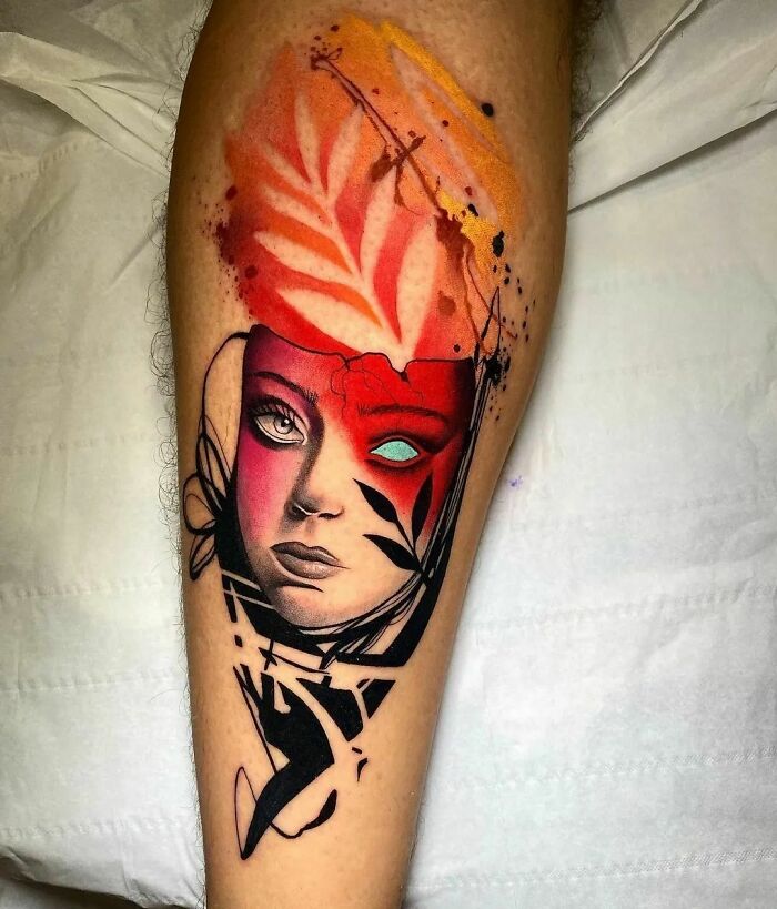 Watercolor tattoo on a leg featuring an abstract face with vibrant red and orange hues.