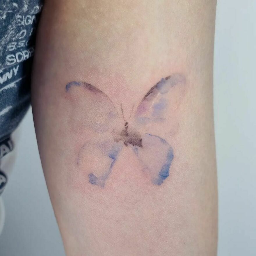Watercolor tattoo of a butterfly on an arm, showcasing a soft, artistic design.