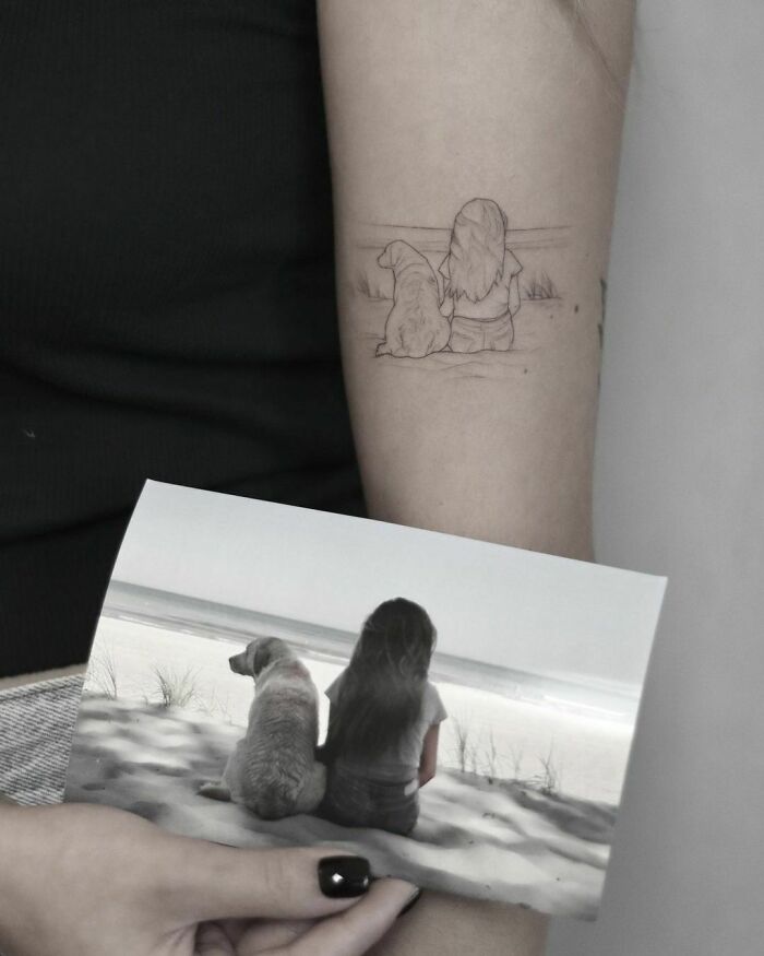 Tattoo of a girl and her dog sitting on the beach, inspired by the photo showing a similar scene, capturing adorable pet bond.