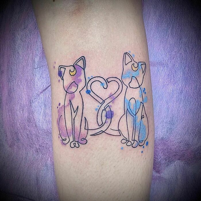 Watercolor tattoo of two cats with moons, tails forming a heart, in purple and blue hues on a light background.