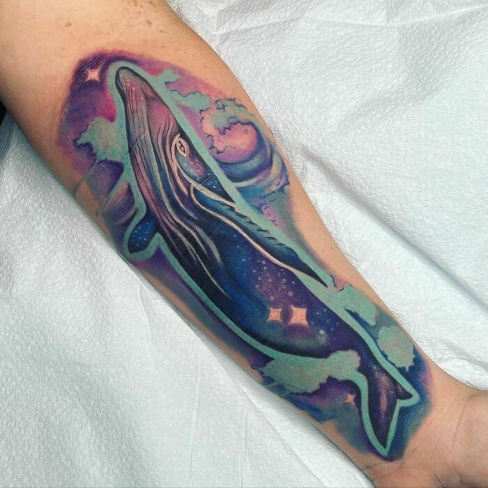 Watercolor tattoo featuring a cosmic whale design, blending vibrant blues and purples on skin for inkspiration.