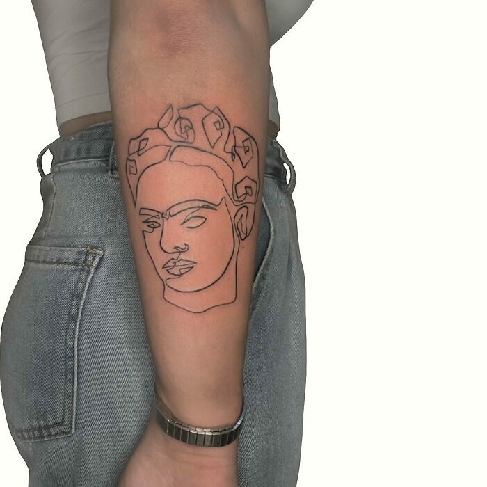 Single-line tattoo of a face on an arm, showcasing intricate artistry in minimalistic design.