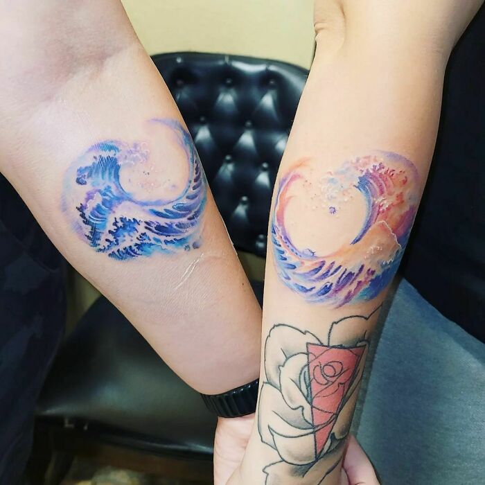 Two forearms with matching watercolor tattoos of ocean waves, showcasing vibrant inkspiration.