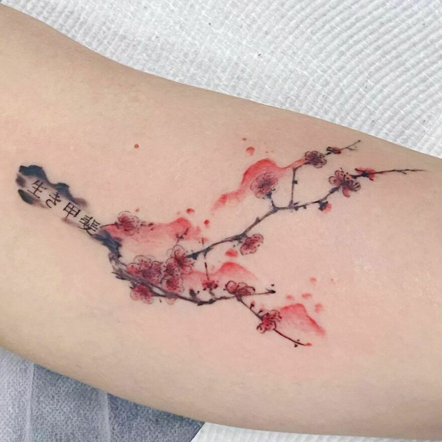 Watercolor tattoo of cherry blossoms with delicate red and black ink on skin.