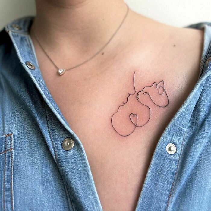 Minimalist single-line tattoo of two abstract faces on a woman's chest, showcasing fine-line artistry.