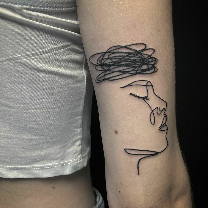 Minimalist line tattoo of a face with scribbles on an arm, showcasing unique tattoo art.