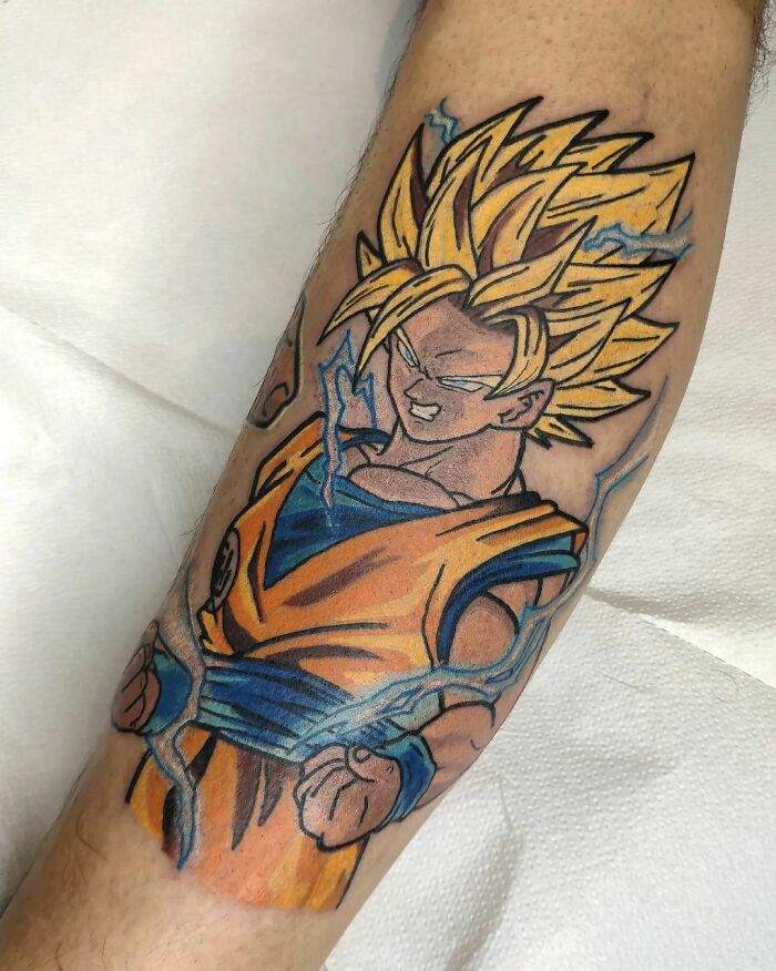 Cartoon tattoo inspired by animated shows, featuring a character with spiky yellow hair and blue aura on a forearm.