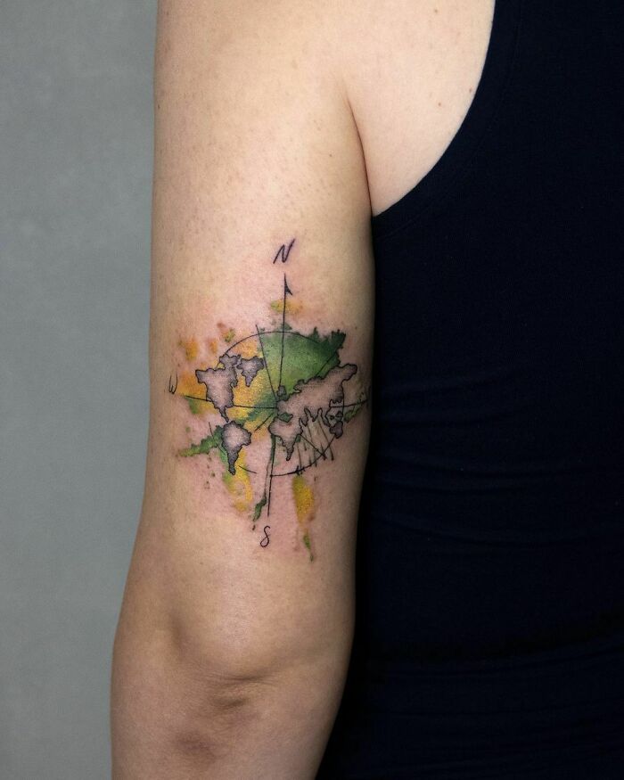Watercolor tattoo of a world map with compass design on an upper arm, showcasing vibrant inkspiration.