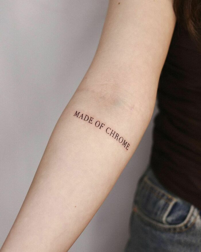 Close-up of an arm with a "MADE OF CHROME" word tattoo, related to meaningful word tattoos.