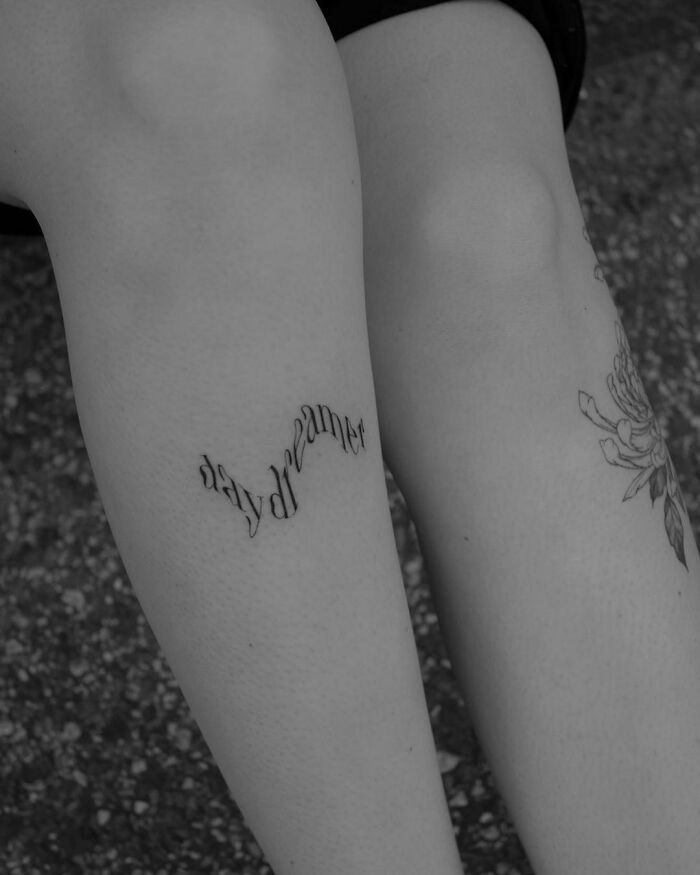 Word tattoo on a leg reading "daydreamer," showcasing creative inkspiration.