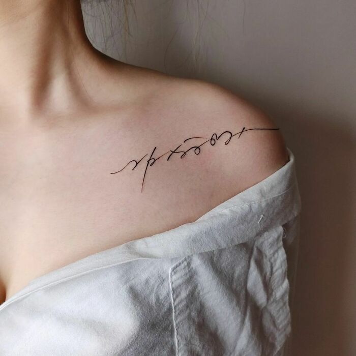 Minimal script word tattoo on a woman's shoulder, showcasing elegant ink design ideas.