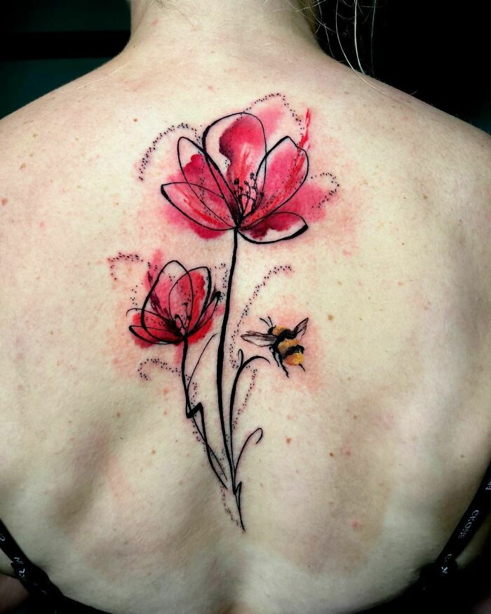 Watercolor tattoo of pink flowers and a bee on a person's back, blending vibrant colors and delicate outlines.