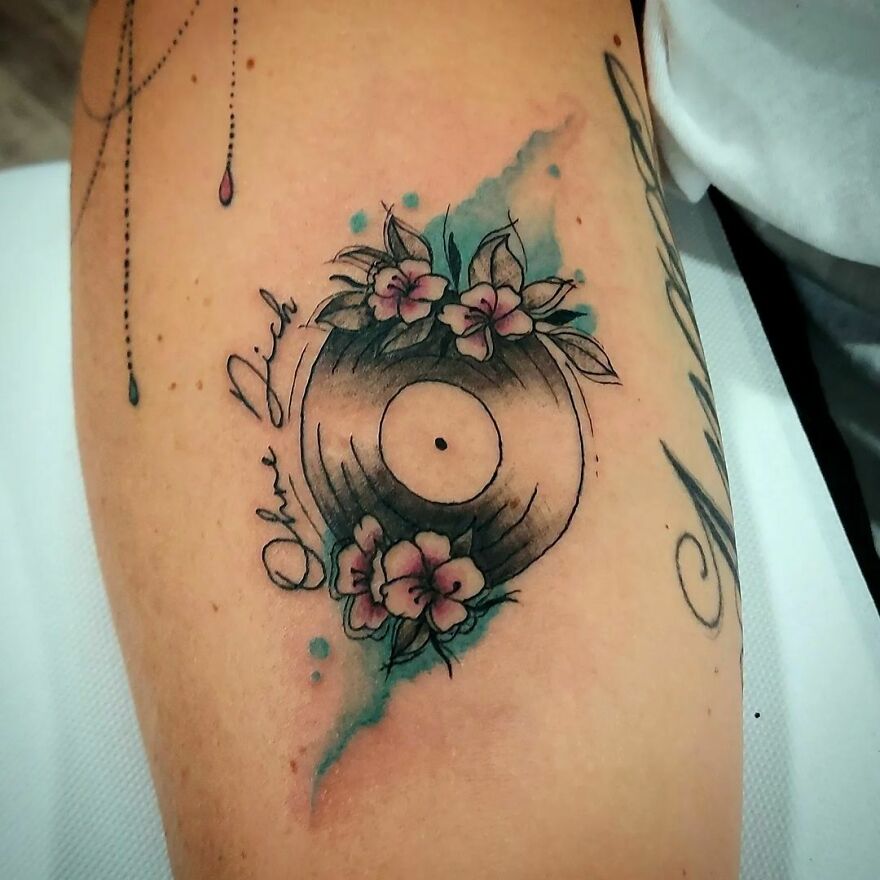 Watercolor tattoo of a vinyl record with flowers and blue accents on an arm.