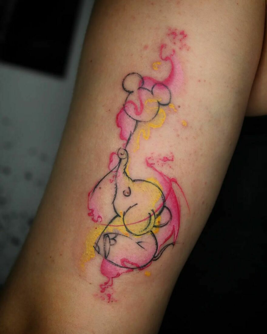 Colorful elephant watercolor tattoo on arm with pink and yellow splashes.