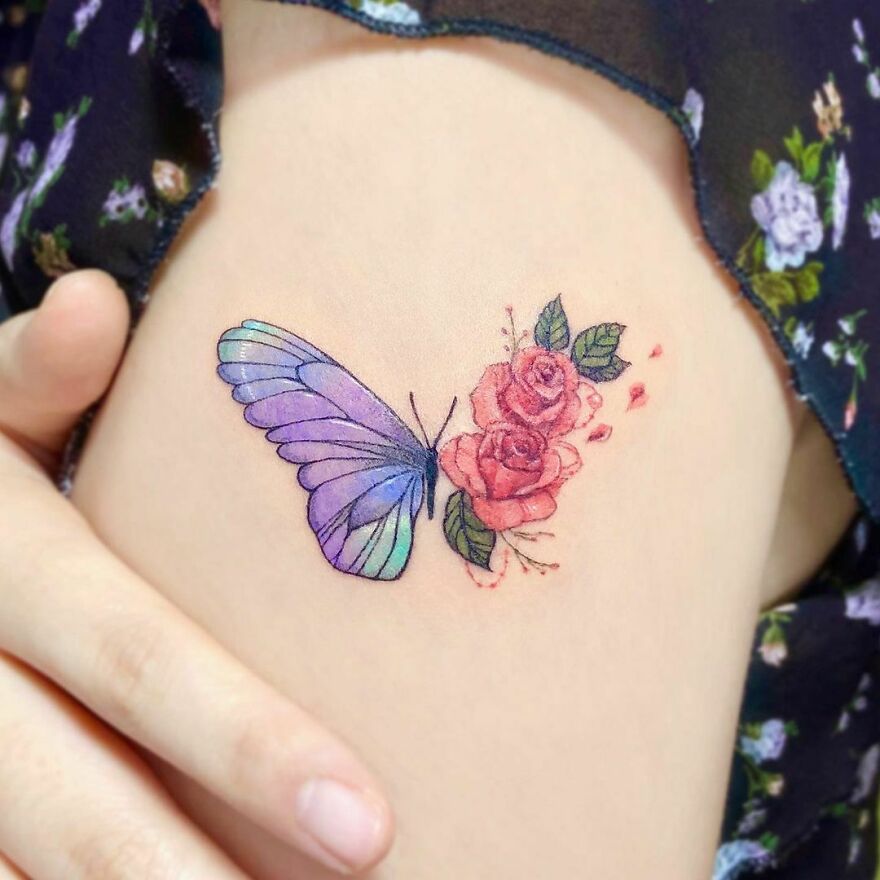 Watercolor tattoo of a butterfly and roses in purple and pink on skin.