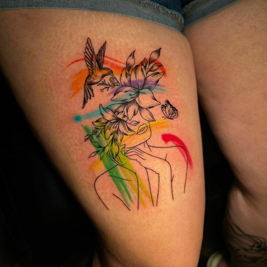 Watercolor tattoo on thigh featuring flowers, a bird, and a butterfly with vibrant colors.