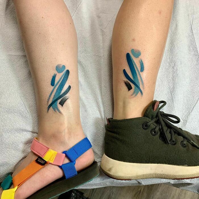 Watercolor tattoos on legs featuring abstract blue and black brushstrokes, with colorful sandals in view.